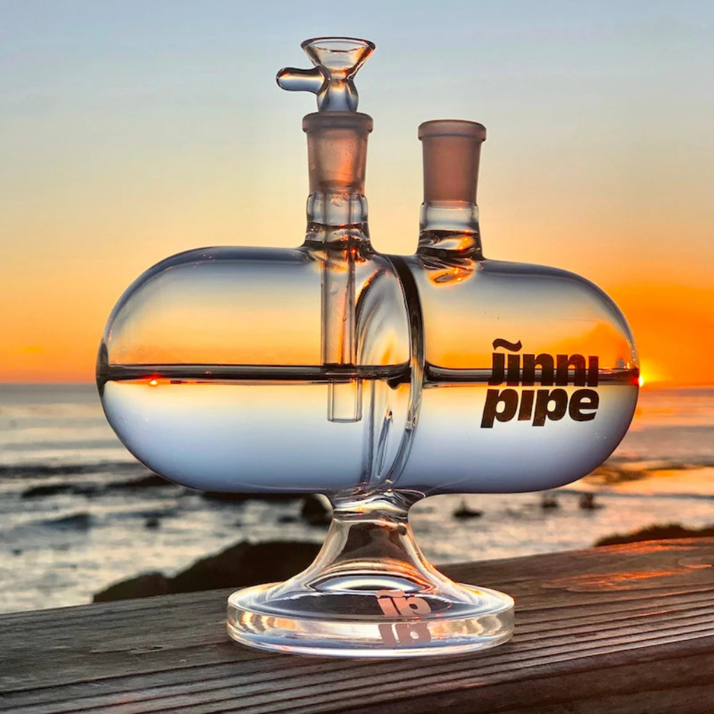 Glass pipe with 'jinni pipe' branding against a sunset ocean backdrop