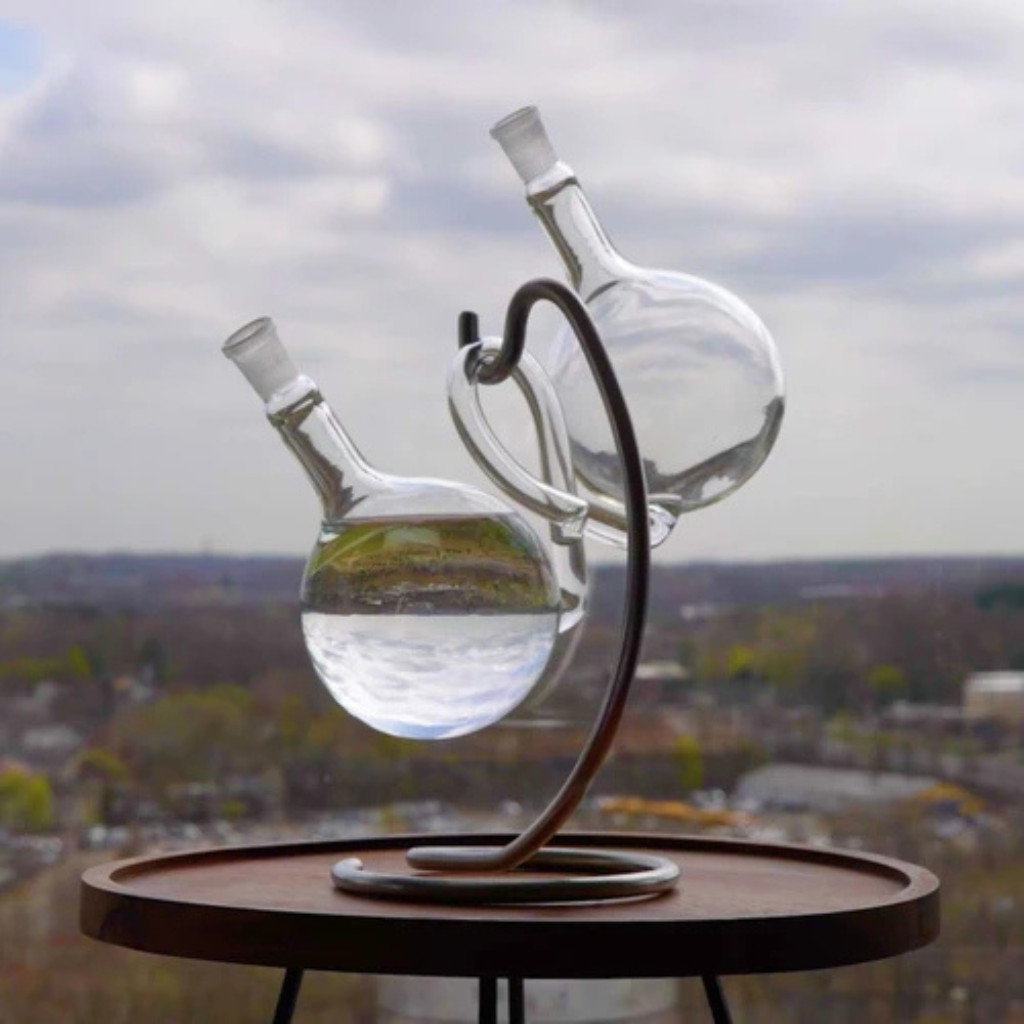 Glass SyphonAir with water on a stand against a cityscape background