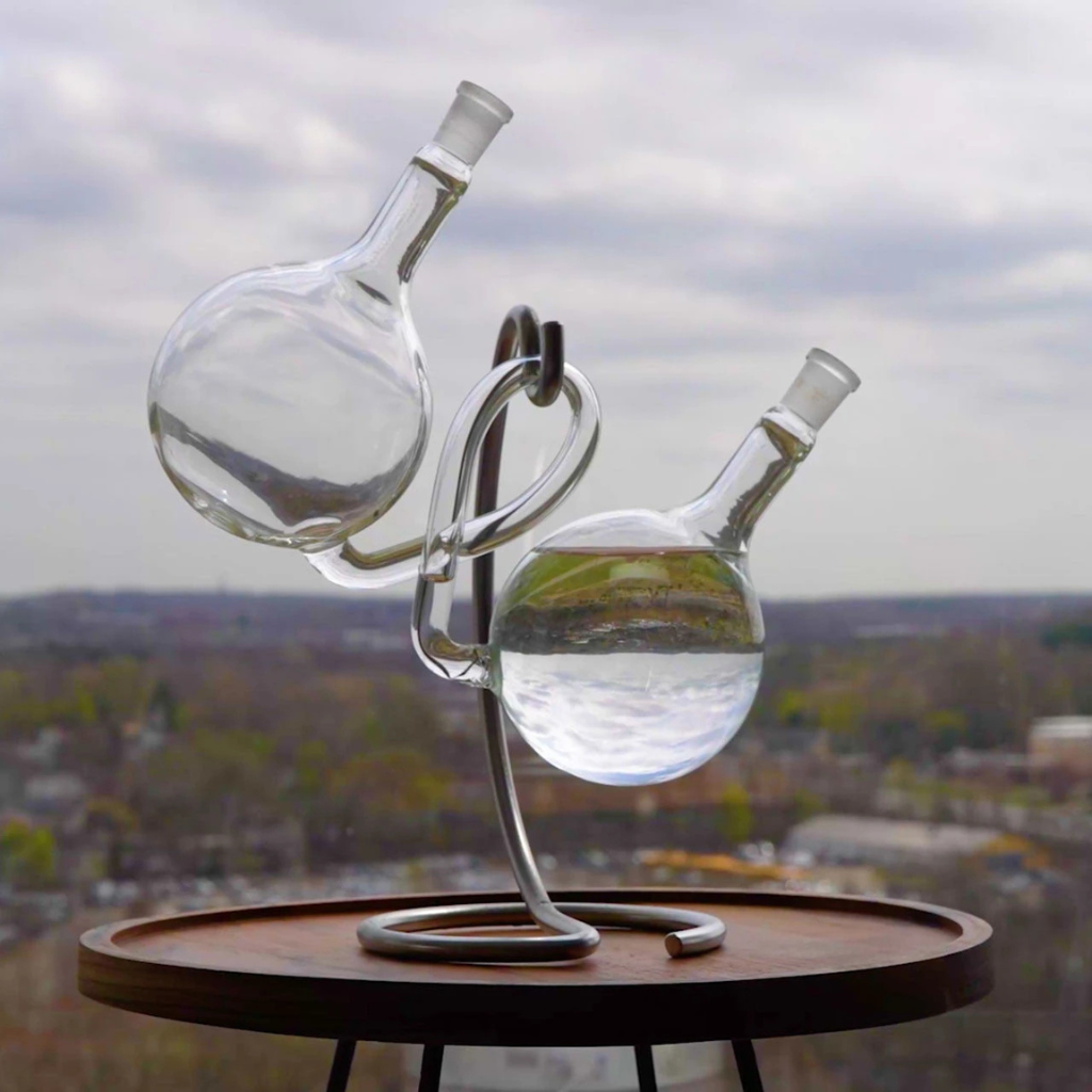 Glass water sculpture on a wooden table with a cityscape background