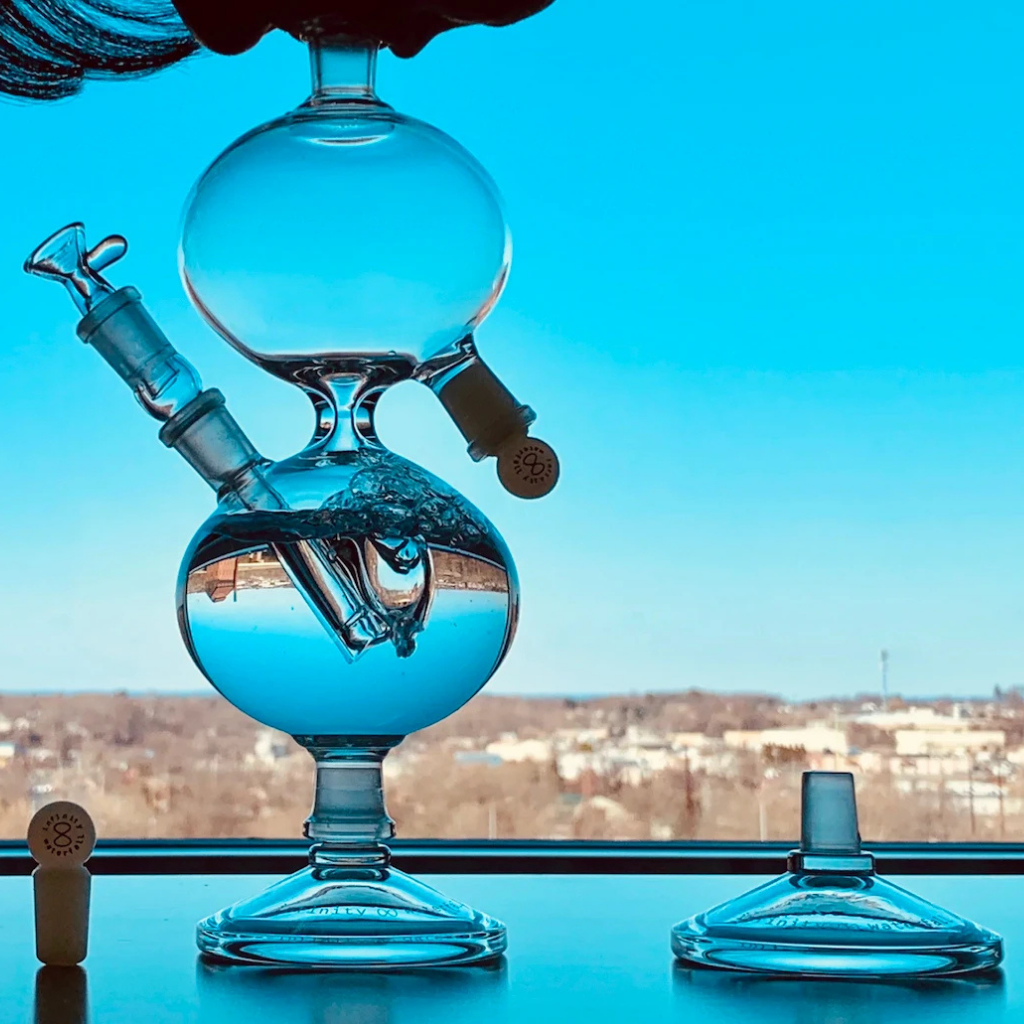 Glass water pipe with blue liquid on a reflective surface, blurred cityscape in the background